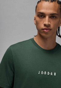 Camiseta de algodón verde con mangas cortas, cuello redondo, con letras claras que dicen "JORDAN" en el pecho. Textura suave.
