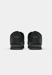 Paire de baskets noires pour hommes vues de dos, avec un talon surélevé et un logo discret de la marque sur l'onglet du talon.