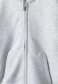 Siva zip-up dukserica s mekim, teksturiranim materijalom, sa središnjim zatvaračem i prednjim džepovima. Nema vidljivih uzoraka ili akcenta.