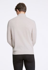 Maglione lavorato a maglia beige con colletto alto, maniche lunghe e vestibilità comoda. La texture appare morbida e liscia, con dettagli a coste nell'orlo.