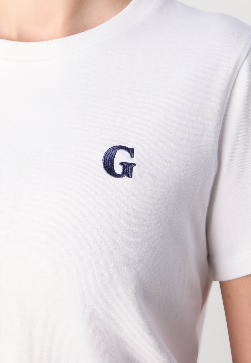 Weißes Baumwoll-T-Shirt mit einem navyblauen, gestickten "G"-Logo auf der linken Brust, Rundhalsausschnitt und kurzen Ärmeln.