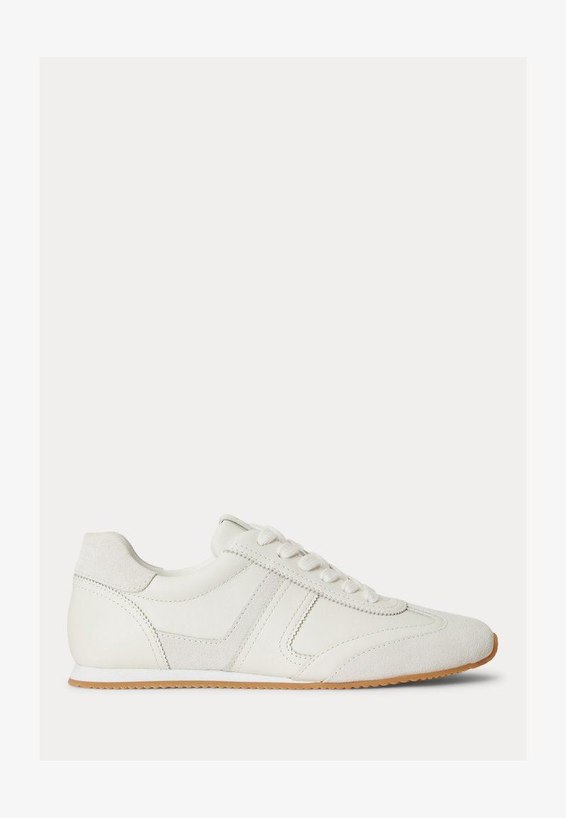 Άσπρο χαμηλό sneaker με κορδόνια, υφασμένα πλαϊνά πάνελ και σόλα από καουτσούκ πάνω σε λευκό απλό φόντο.