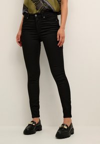 Svarta slim-fit jeans med fem fickor, med silverdetaljer och hög midja. Kombinerat med en mönstrad grön topp och svarta loafers.