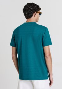 Chemise turquoise à manches courtes avec un motif texturé subtil, un ourlet droit et des fentes latérales. Le design classique du col complète le style.
