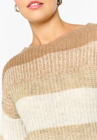 Adīts džemperis ar plašām horizontālām svītrām bēšā, krēmkrāsā un gaiši brūnā krāsā, ar ribotu tekstūru un off-shoulder kakla izgriezumu.