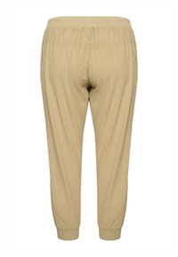 Bež hlače zoženjene navzdol z elastičnim pasom in manšetami, z gladko teksturo in lahkim materialom. Brez vidnih žepov ali okraskov.