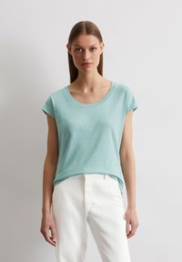 Licht aqua kleurige t-shirt met korte mouwen en een ronde hals, gemaakt van een zachte stof; gecombineerd met witte broek. Eenvoudig ontwerp, geen zichtbare patronen of accenten.