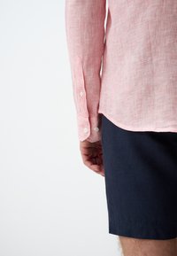 Rot-weiße gestreifte Langarmshirt mit geknöpften Manschetten, kombiniert mit dunkelblauen Shorts. Sichtbare Nähte und Stofftexturdetails.