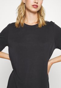 T-shirt preto de manga curta com decote redondo e textura suave, apresentando detalhes de costura discretos nas mangas e laterais.