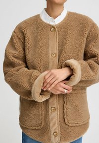 Brun fleecejacka med strukturerad yta, med en kordflorsfrontpanel, knappstängningar och rullade ärmslut.