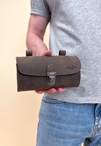 Hnedá kožená peňaženka so zipsom, kovovým uzáverom a prešívanými okrajmi, držaná v ruke osoby. Má dva malé pútka na opasok.
