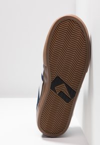 Navy sneaker featuring a rubber sole with herringbone pattern, brown accents, and a black logo detail on the side.
