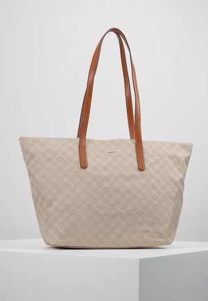 Sac fourre-tout beige avec un motif circulaire subtil, doubles anses d'épaule en cuir marron, et logo de marque argenté sur le devant, présenté sur un piédestal blanc.