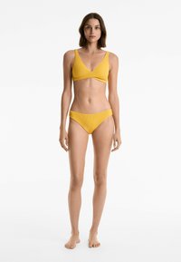 Set di bikini giallo con motivo texturizzato a coste. Il top presenta un profondo scollo a V e spalline larghe, abbinato a slip bikini a vita bassa.