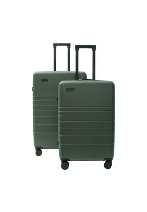 Two dark green hard-shell suitcases with four wheels and extended handles, one larger behind the smaller, standing upright on a white background.