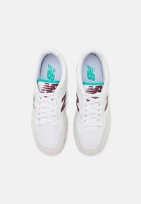 Weiße Sportschuhe mit Obermaterial aus Mesh und Wildleder, ausgestattet mit einem burgunderfarbenen New Balance-Logo, türkisfarbenen Akzenten und traditionellem Schnürdesign.