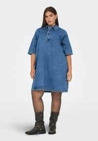 Denimová košilová šaty s límečkem, polovičními rukávy a knoflíkovou légou. Mají uvolněný střih a viditelné stehy na spodním okraji.