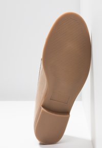 Semelle d'une chaussure beige avec de fines rainures horizontales, talon carré, et taille 37 marquée sur la semelle en caoutchouc.