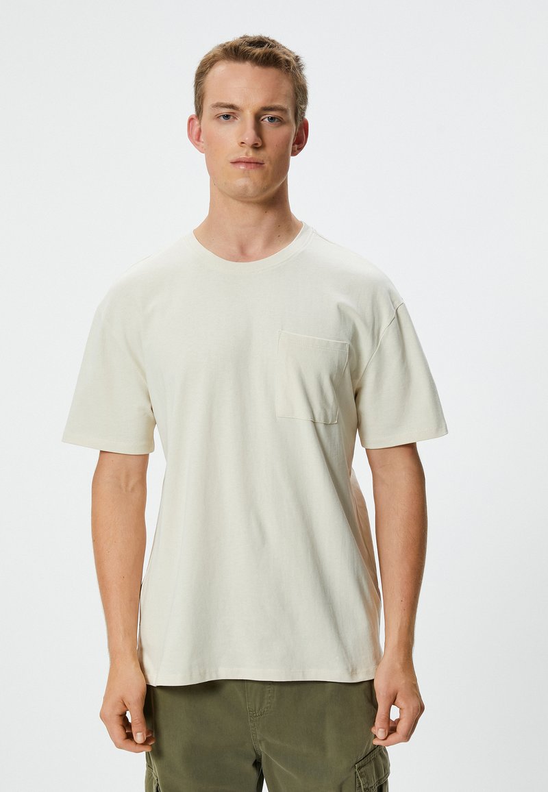 Krämfärgad bomulls-T-shirt med rund halsringning och korta ärmar. Har en liten bröstficka och en avslappnad passform.