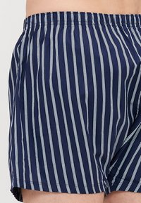 Boxeri bleumarin cu dungi verticale albe, talie elastică, material ușor și o croială confortabilă, având un design cu picioare largi.