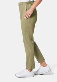 Khaki-Hosen mit elastischem Bund, schmaler Passform, Seitentaschen und Schlitzsaum, kombiniert mit weißen Sportschuhen.
