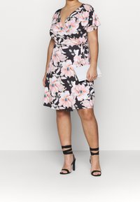 Kwiatowa sukienka kopertowa z krótkimi rękawami, z różowymi i niebieskimi kwiatami na ciemnym tle. Dobrana z czarnymi sandałami na szpilce i białą kopertówką.