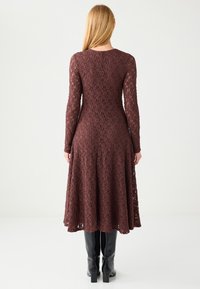 Brązowa koronkowa sukienka z długim rękawem, z rozkloszowanym dołem, misternym wzorem i subtelną fakturą, zestawiona z czarnymi kozakami za kolano.