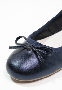 Gros plan d’une ballerine bleu marine à bout arrondi avec un petit nœud décoratif à l'avant.