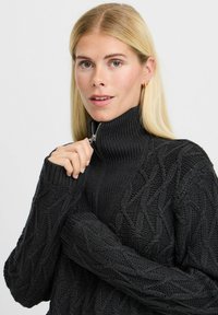 Schwarzer gestrickter Rollkragenpullover mit einem strukturierten Rautenmuster, ausgestattet mit einem Reißverschluss am Kragen und gerippten Bündchen.