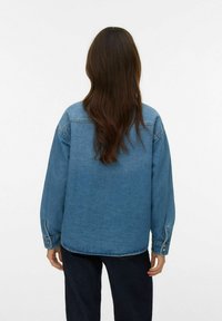 Giacca di jeans di un blu chiaro con vestibilità rilassata, caratterizzata da maniche lunghe, polsini a bottoni e orlo curvo. Vista posteriore che mostra una texture liscia.