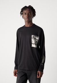 Zwarte t-shirt met lange mouwen van katoen, voorzien van een witte grafische opdruk op de borstzak en tekstaccenten op de mouw. Soepele textuur en een ontspannen pasvorm.