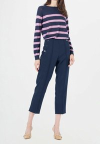 Pantalon taille haute bleu marine avec des accents de boutons dorés et une coupe sur mesure, associé à un pull rayé violet et bleu marine.