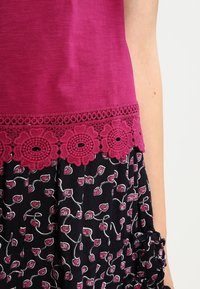 Top fucsia con ribete de encaje y tela oscura con patrones florales rosas. El diseño incluye detalles de croché en el dobladillo.