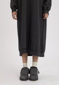 Lang, donkergrijze, oversized jurk van zachte stof, met geribde manchetten en zoom. Gecombineerd met robuuste grijze sneakers en witte sokken.
