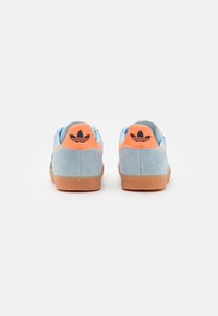 Blue suede sneakers with an orange heel counter. Logo detail in black on the heel. Gum rubber sole, classic design with textured grip.