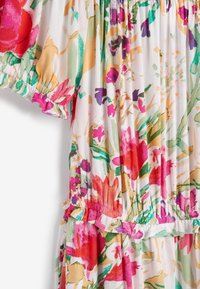 Bloemenjurk met een witte achtergrond en meerkleurige bloemen in roze, rood en groen. Met ruches aan de mouwen en een gerimpelde taille.