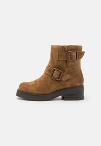 Brown suede ankle boot with two decorative buckles, rounded toe, and a chunky dark brown heel. Side stitching detail visible.