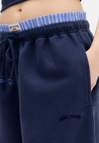 Mornarska trenirka s teksturiranim završetkom, s elastičnom trakicom na struku koja ima plavi karirani uzorak unutrašnjosti, i desnim džepom. BDG JEANS logo izvezen tamnom niti.