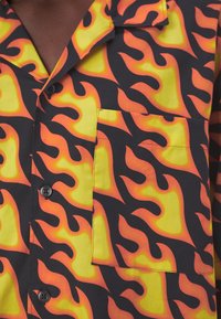 Chemise boutonnée avec motif de flammes vives en jaune, orange et noir, dotée d'une poche poitrine.
