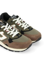 Des baskets avec une tige en textile vert et marron, dotées de lacets blancs, d'un logo blanc et d'une semelle en caoutchouc avec un motif de crans noir.