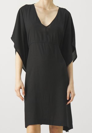 Czarna sukienka o luźnym kroju, z dekoltem w serek i krótkimi rękawami. Miękki materiał z płynnym fasonem i asymetrycznym dołem.