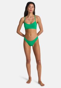 Σετ πράσινου μπικίνι από απαλό υλικό· τοπ μπραλέτα με λεπτές τιράντες, μαγιό κάτω μέρος χαμηλής μέσης με πτυχώσεις στο πλάι.