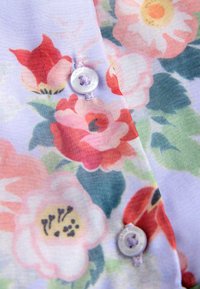 Zbliżenie na kwiecistą tkaninę z różowymi, czerwonymi i żółtymi kwiatami oraz białe guziki przyszyte fioletową nitką.