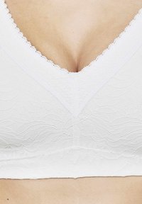 Witte kanten bralette met een diepe V-hals. Gewatteerd bloemenpatroon en geschulpte rand langs de halslijn. Soepele stof en aansluitend ontwerp.