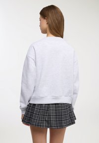 Felpa oversize grigio chiaro con scollo rotondo e orlo a coste, abbinata a una gonna plissettata a quadri neri e grigi.