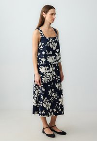 Marineblaues Blumen-Zweiteiler-Outfit, bestehend aus einem ärmellosen Oberteil mit quadratischem Ausschnitt und einem passenden Rock. Leichter Stoff mit auffälligen weißen Mustern.