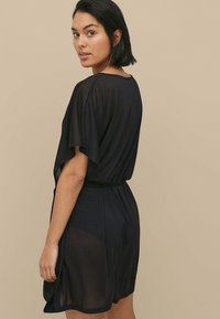 Abito nero fino al ginocchio con maniche corte, realizzato in tessuto leggero e trasparente. Presenta una vita aderente e una vestibilità relax.