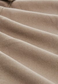 Beige stof met een zachte, gestructureerde oppervlakte, met meerdere diepe plooien die een golfachtig patroon over het materiaal creëren.