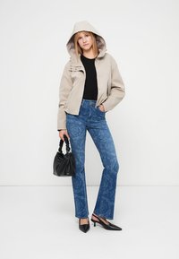 Μπεζ μπουφάν με κουκούλα, μαύρο μπλουζάκι, μπλε τζιν με σχέδιο και φαρδιά άκρα, μαύρη τσάντα και μαύρα μυτερά τακούνια. Απλή, δομημένη σιλουέτα.