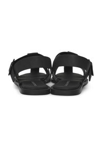 Schwarze Sandalen mit breiten Riemen, offenem Zehendesign, flacher Sohle, verstellbarem Schnallenakzent und glatter Textur.